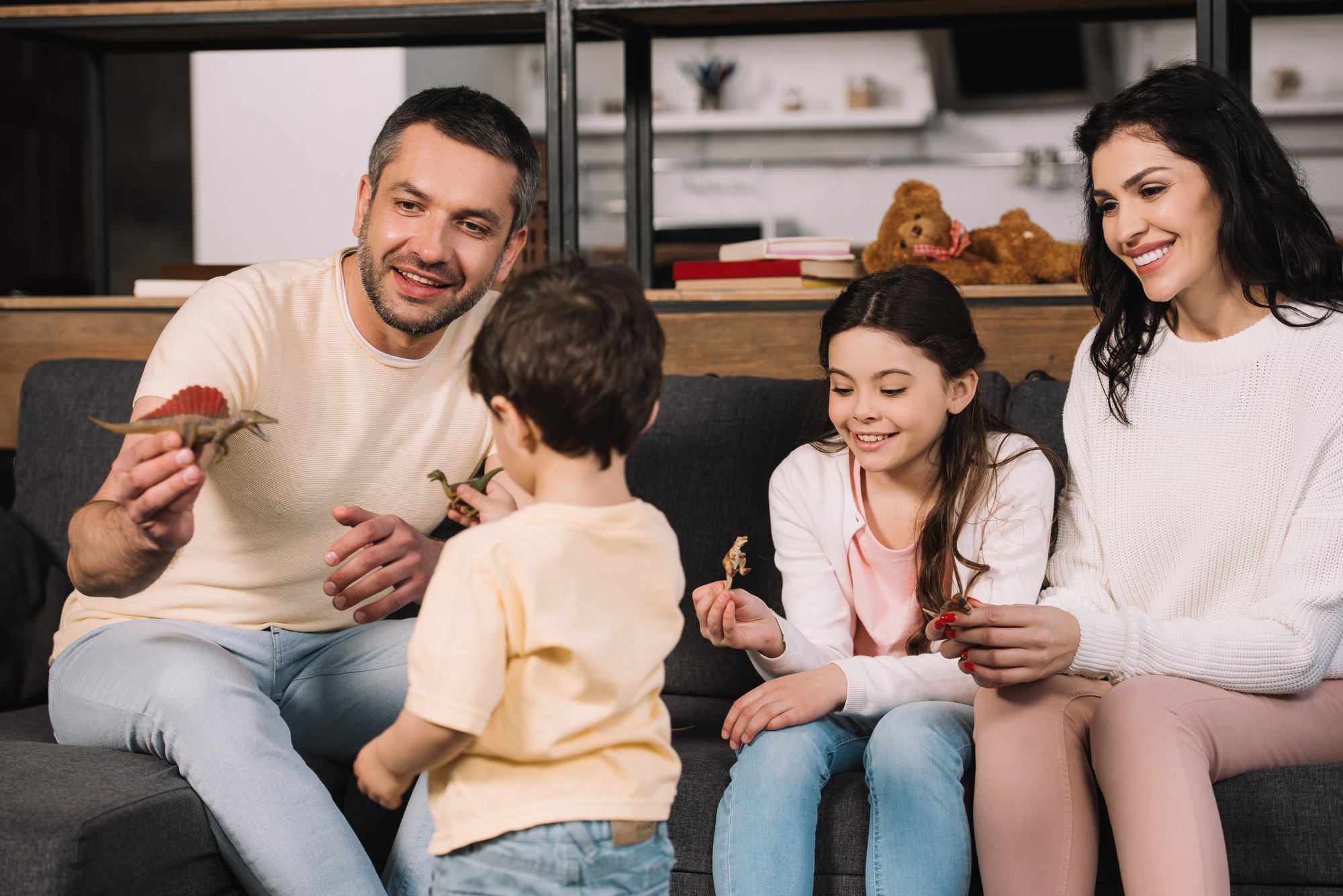 Back view of toddler holding toy near happy parents and sister in living room