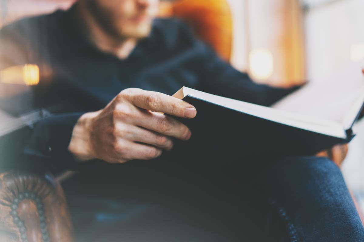 Man sitting in vintage chair university library, reading book and relaxing