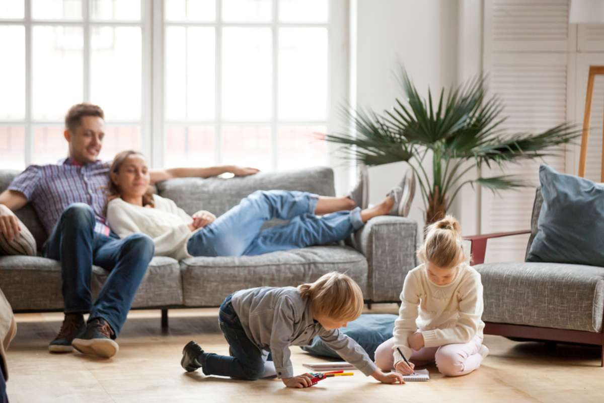 Children sister and brother playing drawing together on floor while young parents relaxing