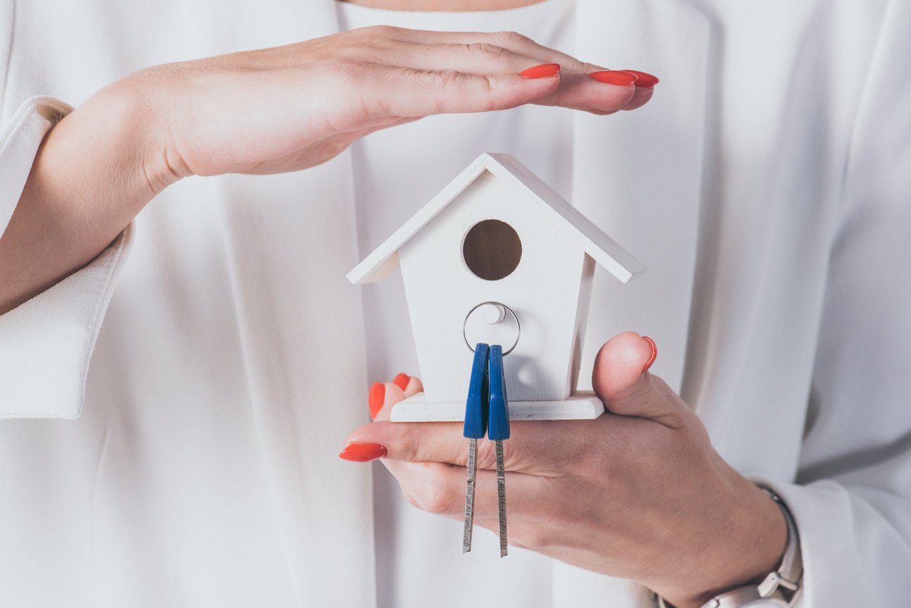 Cropped view of businesswoman holding and covering house model and keys with hand