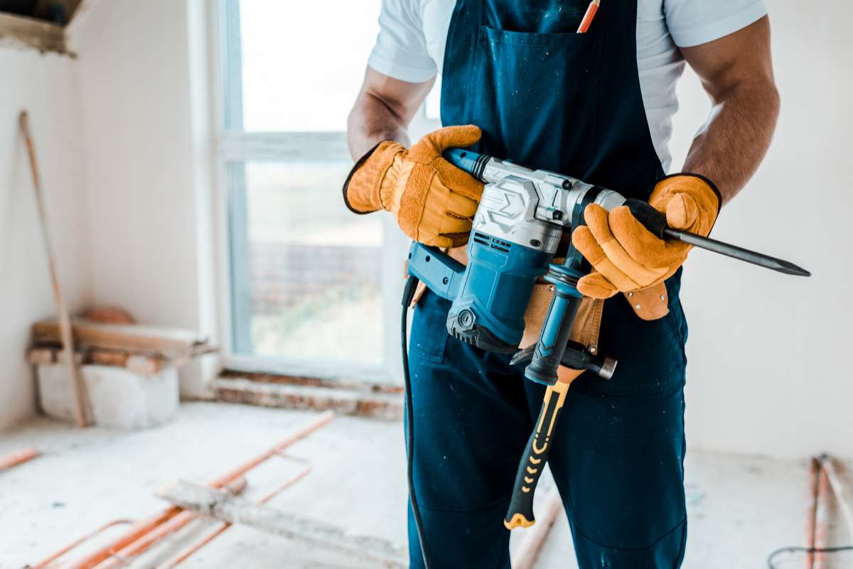 Cropped view of workman in yellow gloves holding hammer drill-1