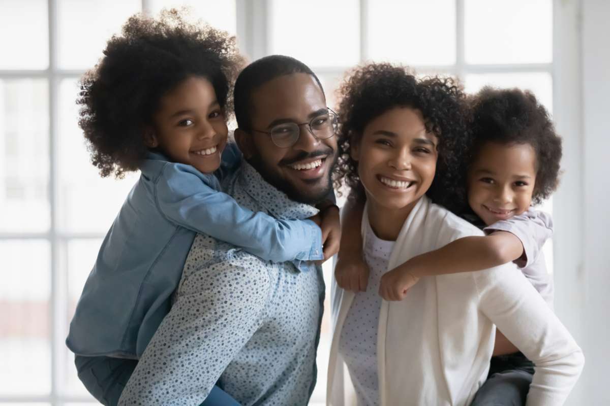 Portrait of African ethnicity parents piggy back son and daughter posing indoors