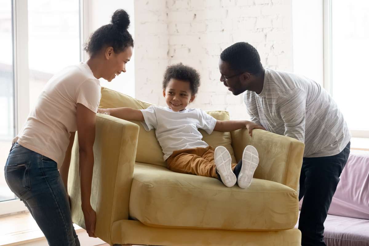 African couple carrying armchair where sit adorable small toddler son