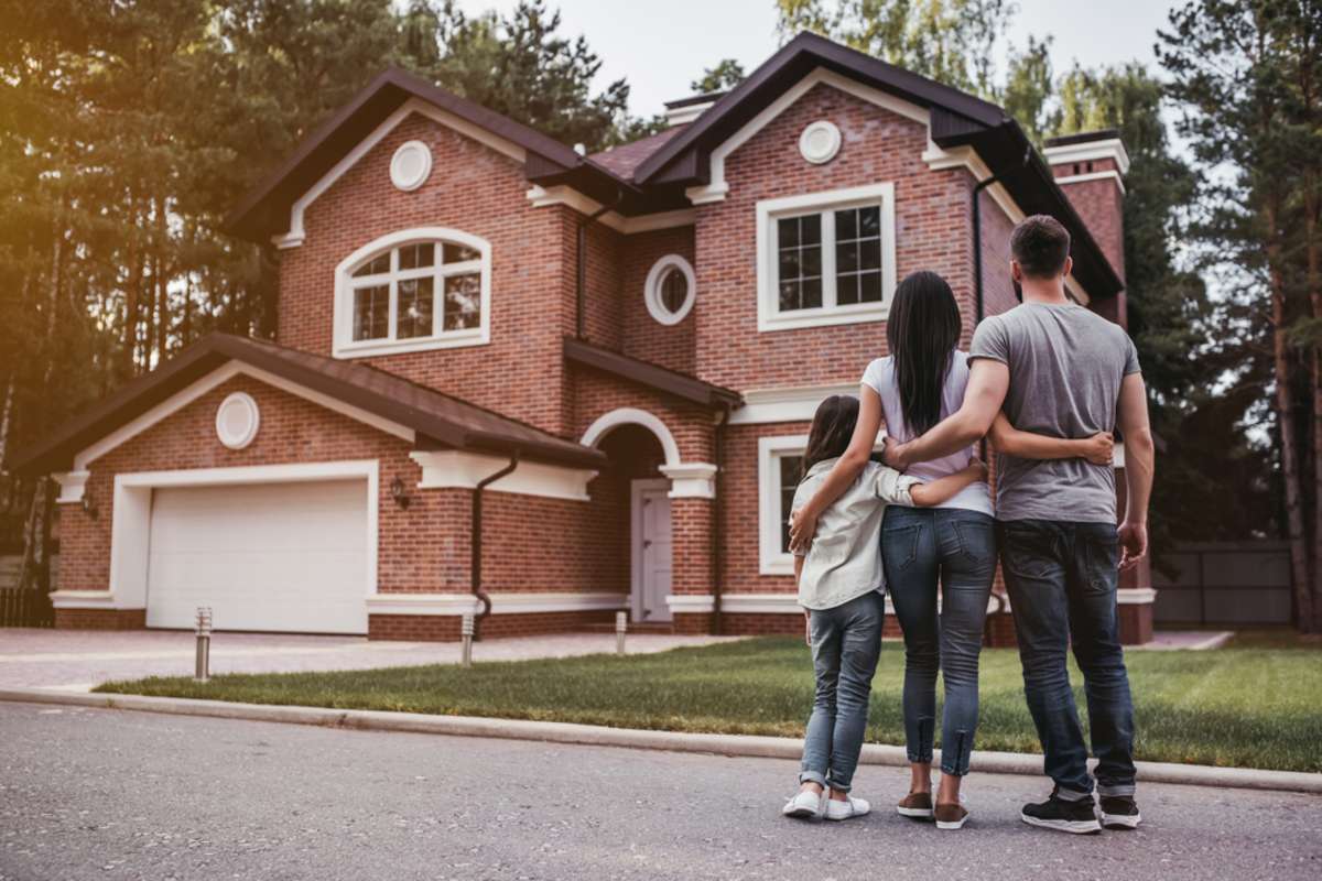 Back view of happy family is standing near their modern house and hugging