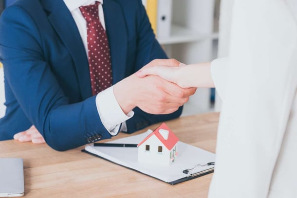Partial view of customer shaking hands with realtor near house model
