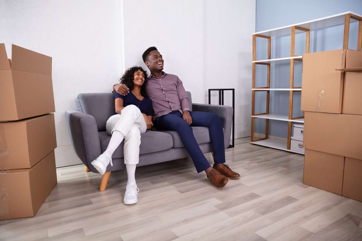 Young Couple Sitting On Couch Inside Their New Home (R) (S)